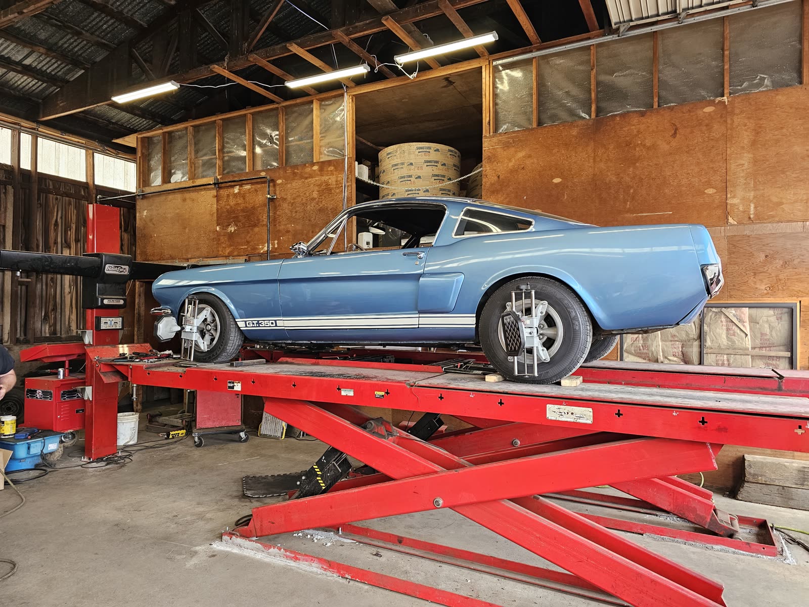 A blue Shelby GT-350 up on the red alignment rack with Hunter alignment heads clamped to its wheels.