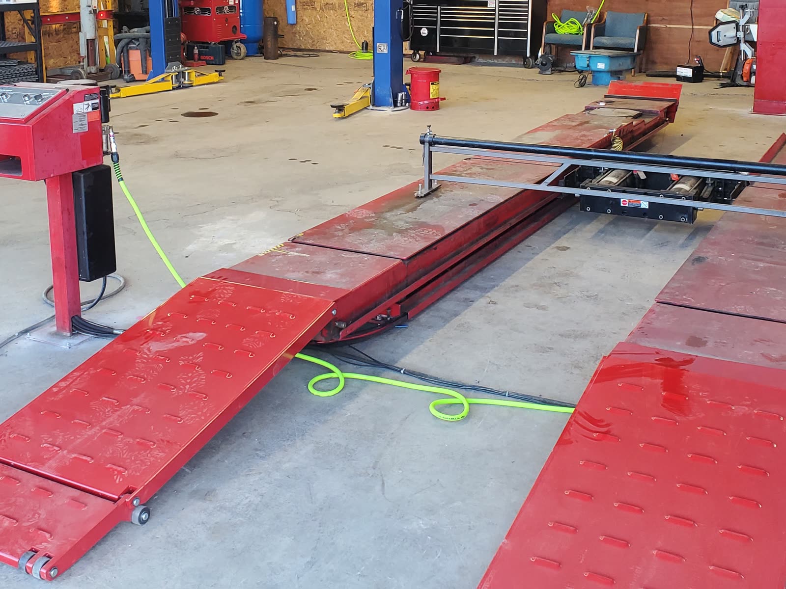 The shop floor, with the red alignment rack and its ramp down, a blue two-post lift and a tool chest behind.